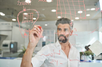 Serious bearded man working and writing on glass wall by . 